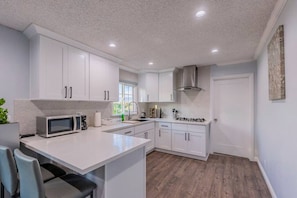 A modern kitchen with white cabinetry, a central island, and a stainless steel range hood. - Stunning LA Luxury Retreat Ideal for Work or Play (Monterey Park)