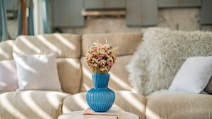 A living room with a beige sofa, a small round table with a blue vase and a book, and a fluffy white throw blanket. - Cozy Family Retreat Game Room Backyard in Hacienda (Hacienda Heights)