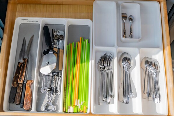 Un cajón con divisiones que contiene varios utensilios de cocina, incluyendo cuchillos, un sacacorchos y palillos.