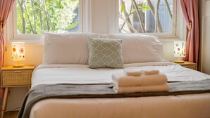 A neatly made bed with a pillow, a bedside lamp, and a window with curtains. - Cozy Family Retreat Game Room Backyard in Hacienda (Hacienda Heights)