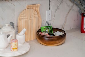 A kitchen counter with a wooden cutting board, a bowl with tea bags, a teapot, a sugar bowl, and a small decorative item. - Cozy Family Retreat Game Room Backyard in Hacienda (Hacienda Heights)
