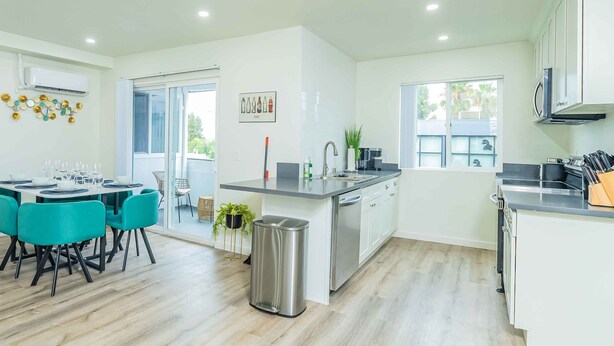 A modern kitchen with a central island, white cabinetry, and a dining area with teal chairs. - Newly Remodeled 2b2b APT Near Pasadena Old Town (Altadena)
