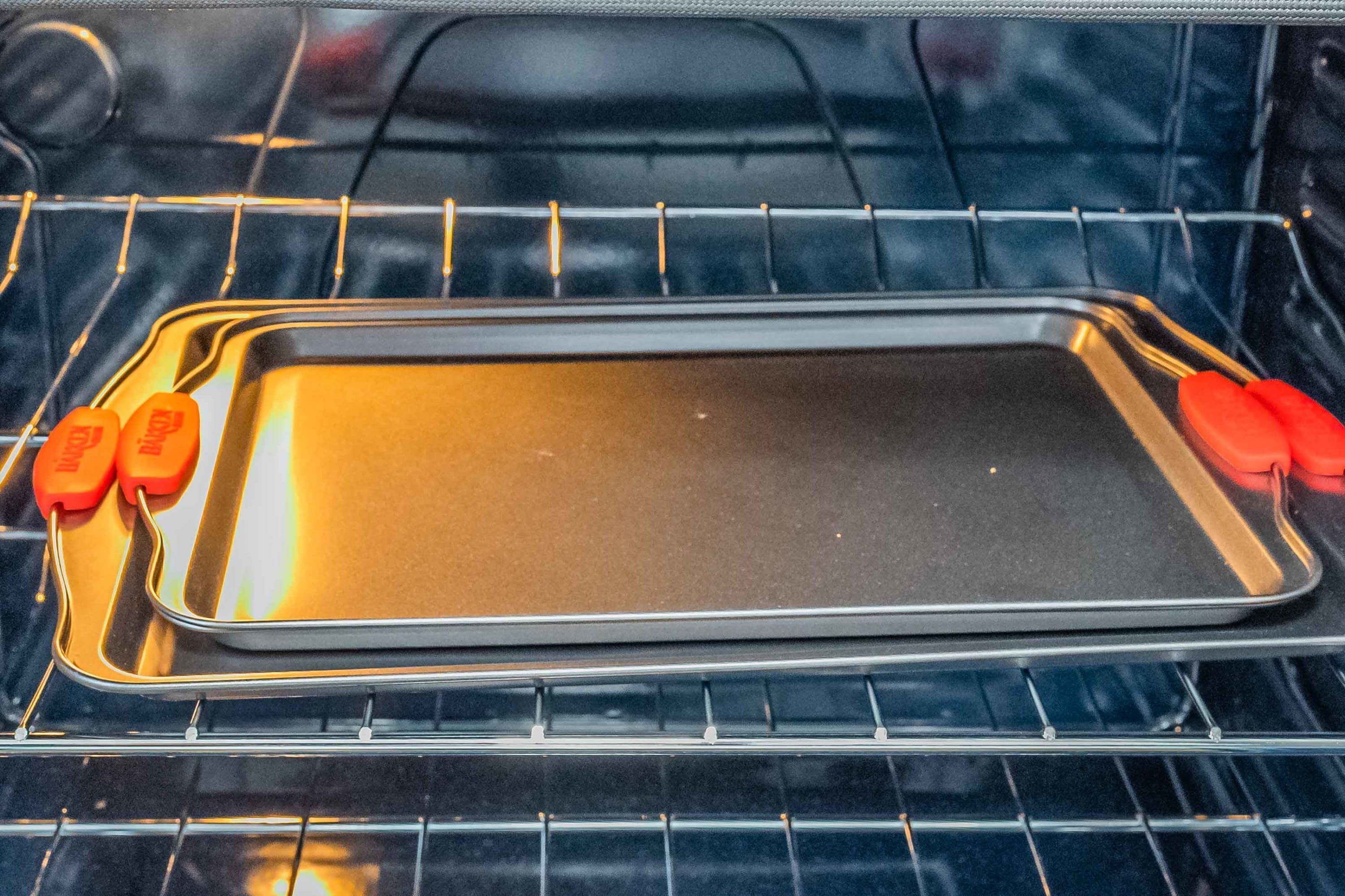 An empty baking tray inside an oven with a wire rack.