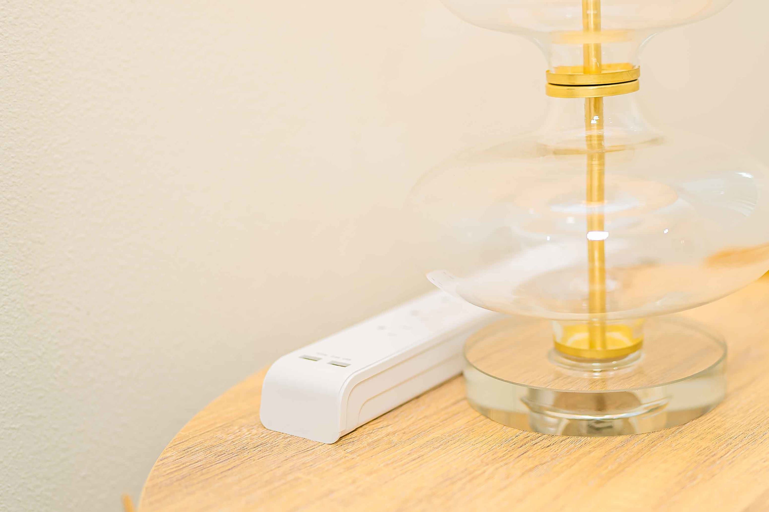 Una lámpara moderna con pantalla de vidrio transparente y base blanca, sobre una superficie de madera.