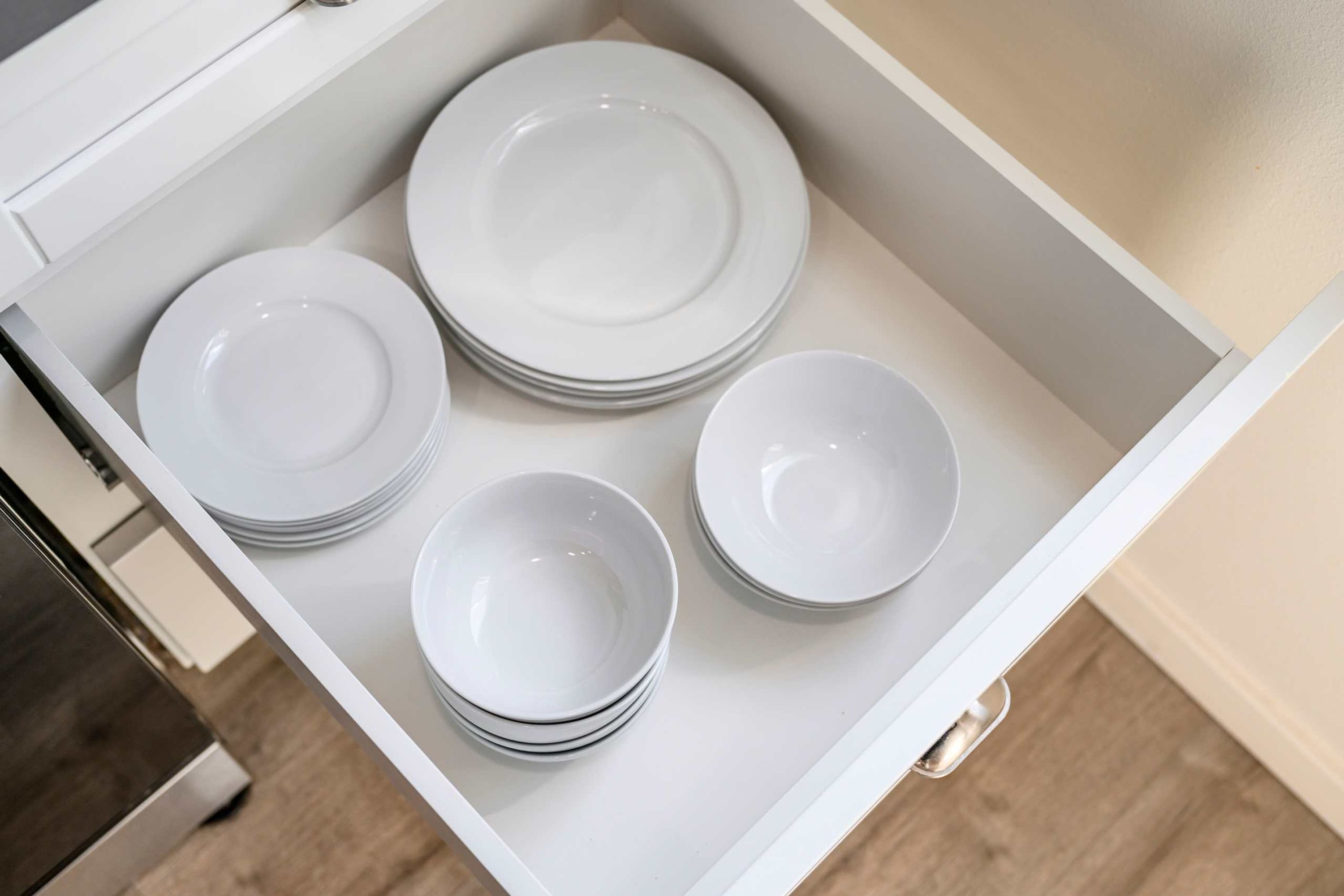 A drawer with neatly stacked white plates and bowls.