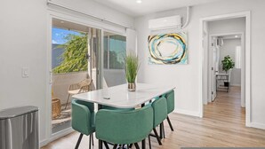 A modern dining area with a white table and green chairs, a potted plant, and a colorful abstract painting on the wall. - Newly Remodeled 2b2b APT Near Pasadena Old Town (Altadena)