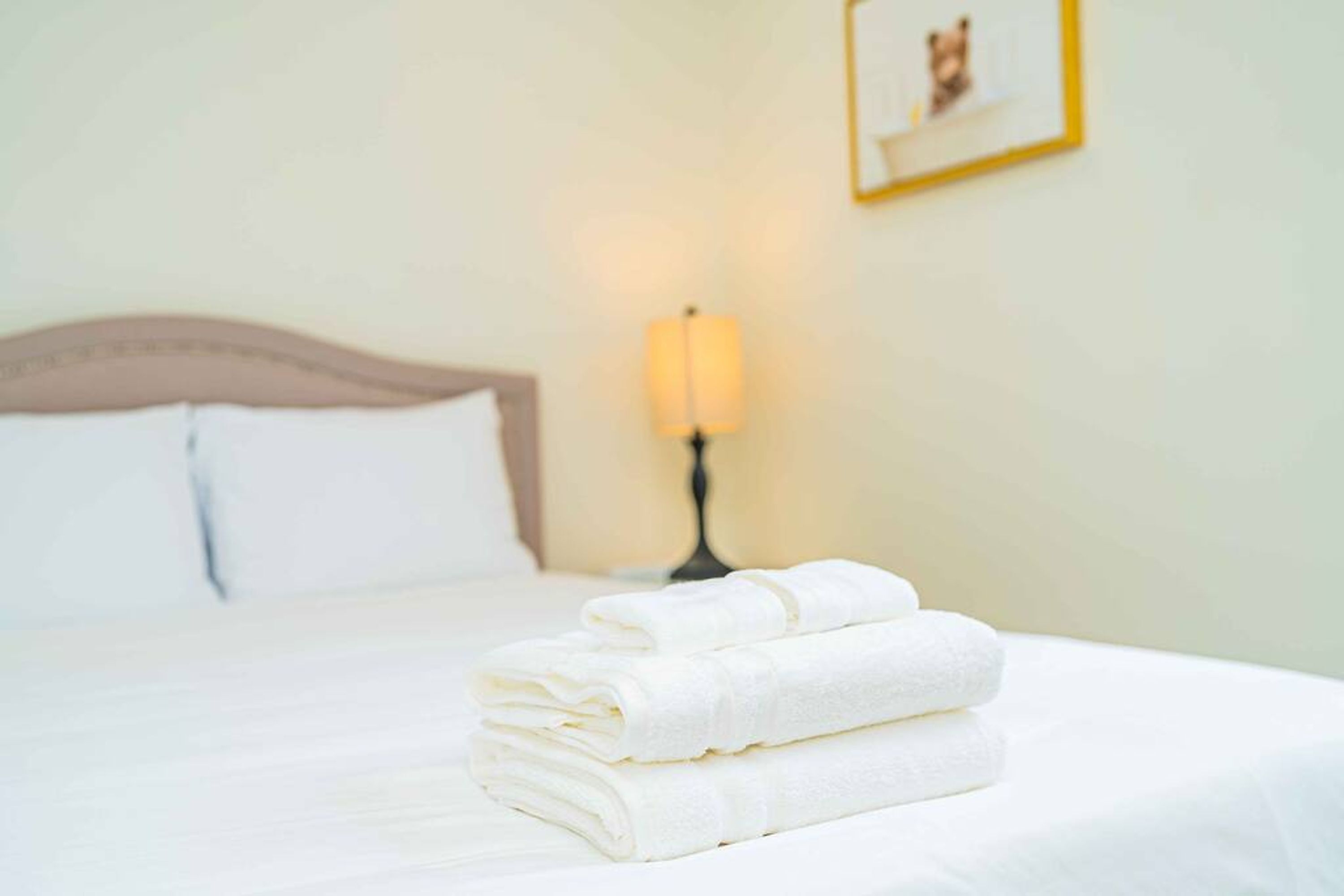 A neatly made bed with folded white towels and a bedside lamp.