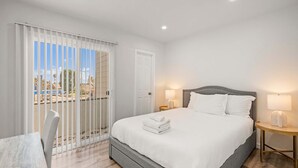 Ein modernes Hotelzimmer mit einem großen Bett, zwei Nachttischen mit Lampen und Meerblick vom Balkon, sowie einem Sessel am Fenster.