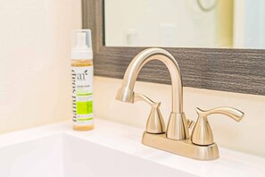 Un bagno con un rubinetto dorato, uno specchio e una bottiglia di disinfettante per le mani sul lavandino.