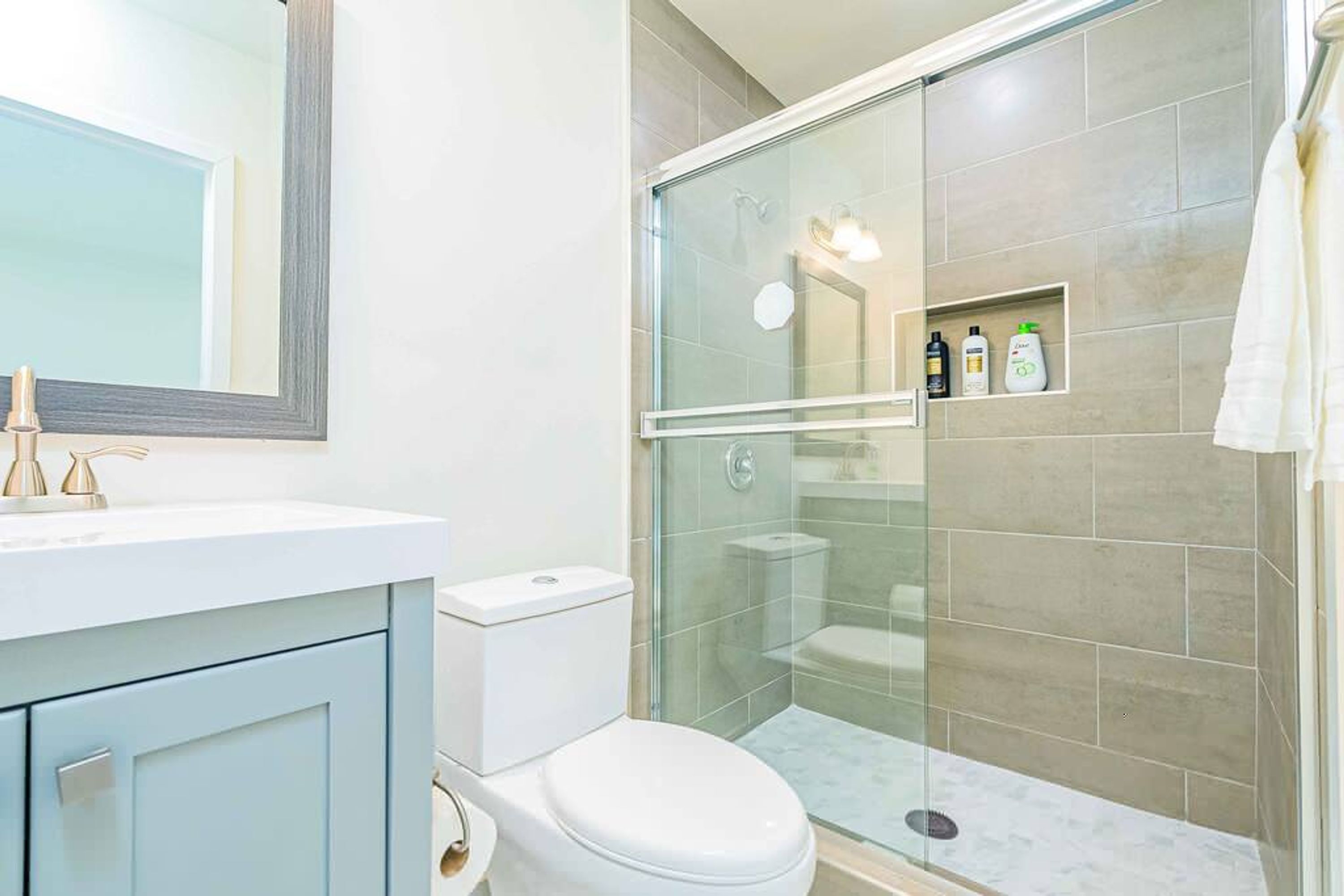 Et moderne badeværelse med bruseniche, hvidt toilet og et spejl med vaskearrangement.