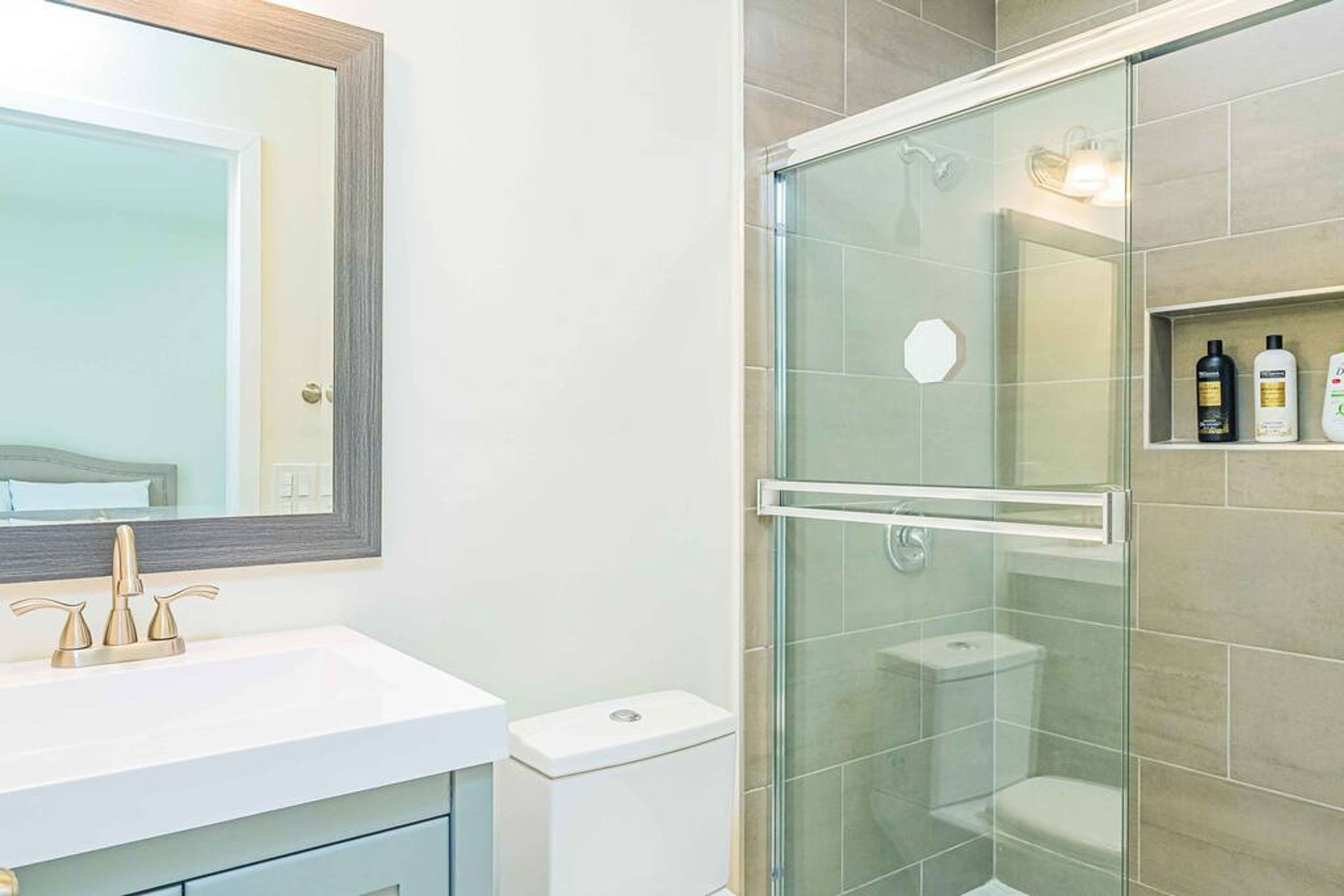 A modern bathroom with a glass-enclosed shower, a white sink with a gold faucet, and a mirror above the sink.