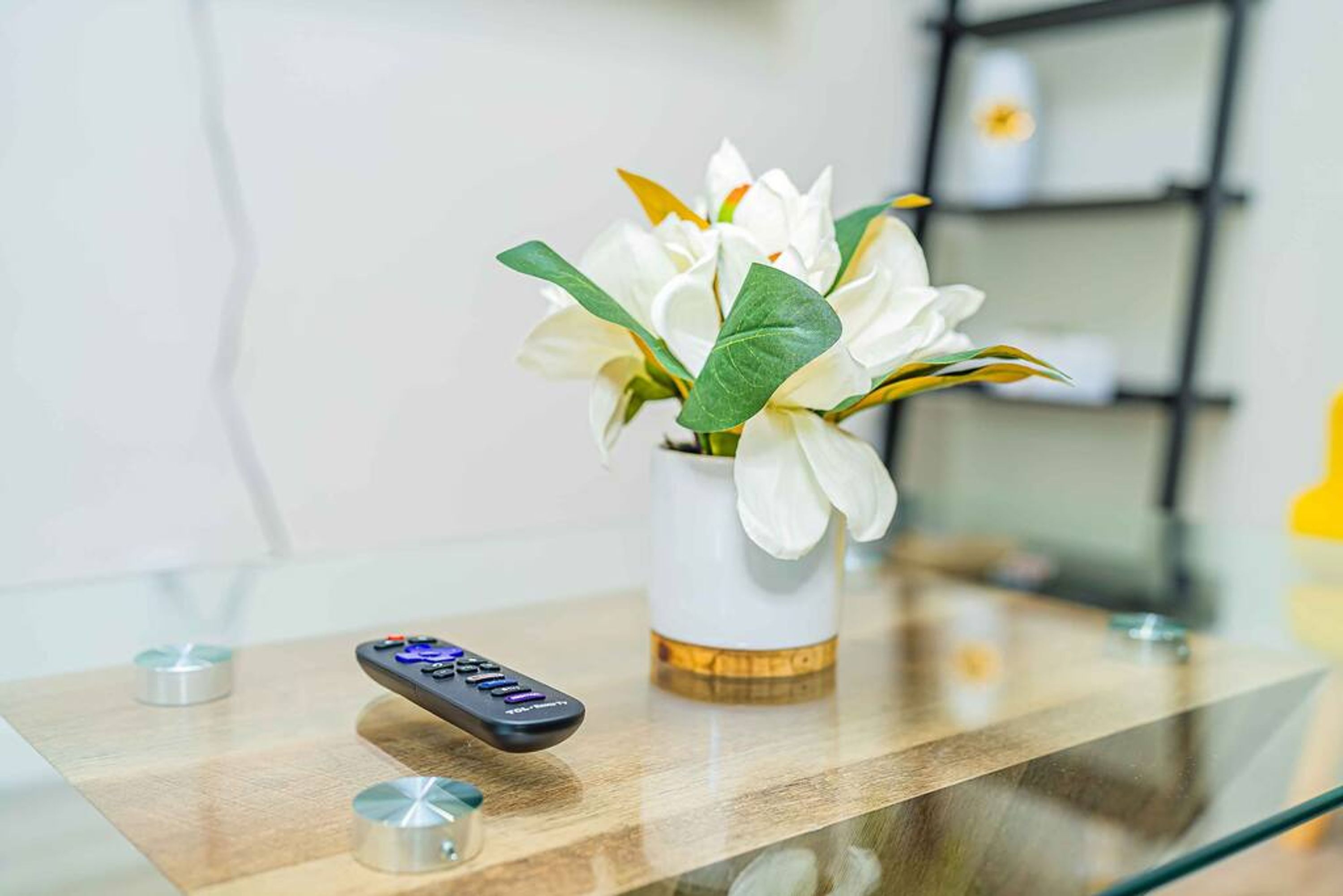 A remote control and a vase with white flowers on a glass table.