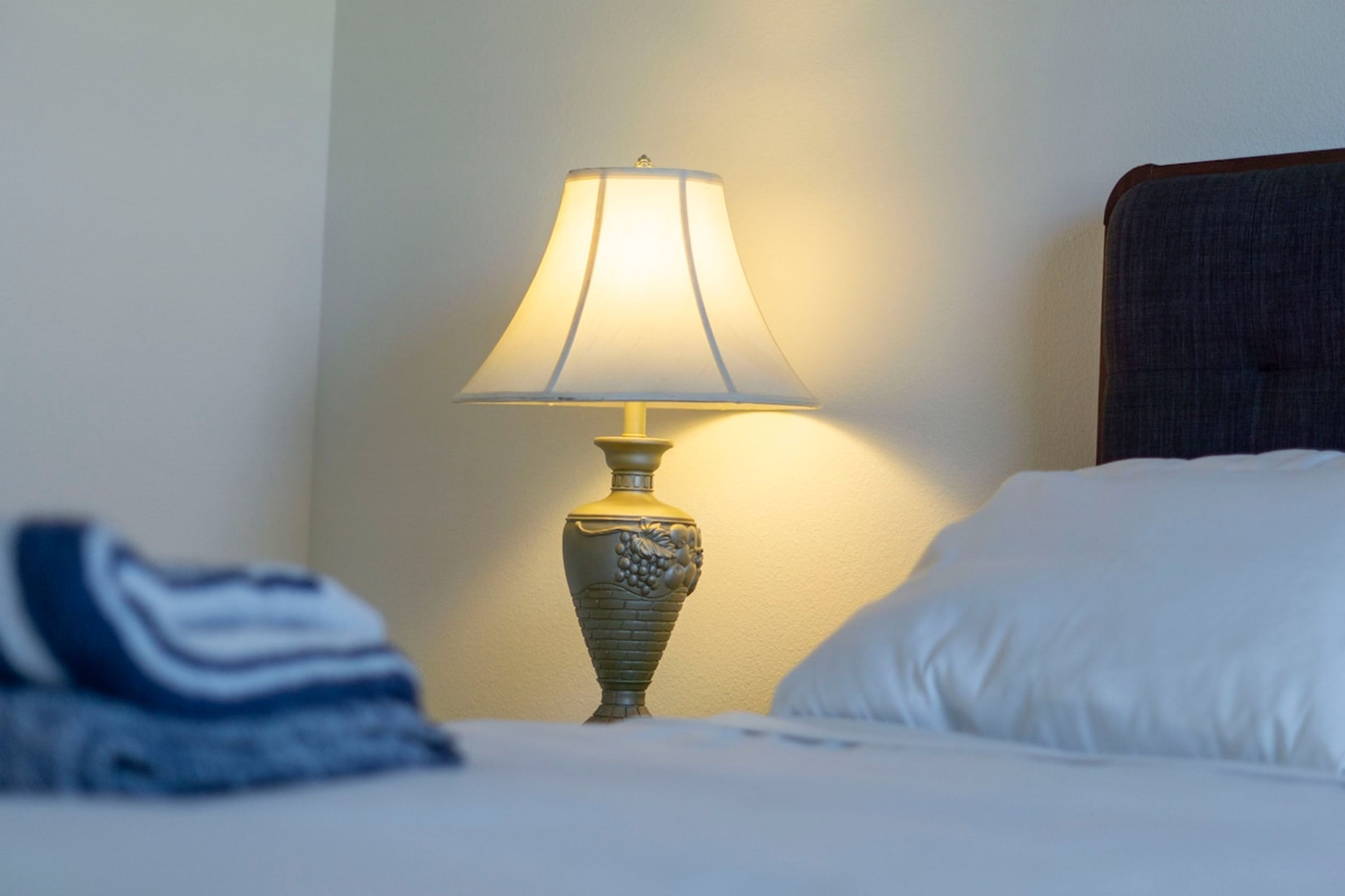 A bed with a white pillow and a lamp with a decorative base on a bedside table.