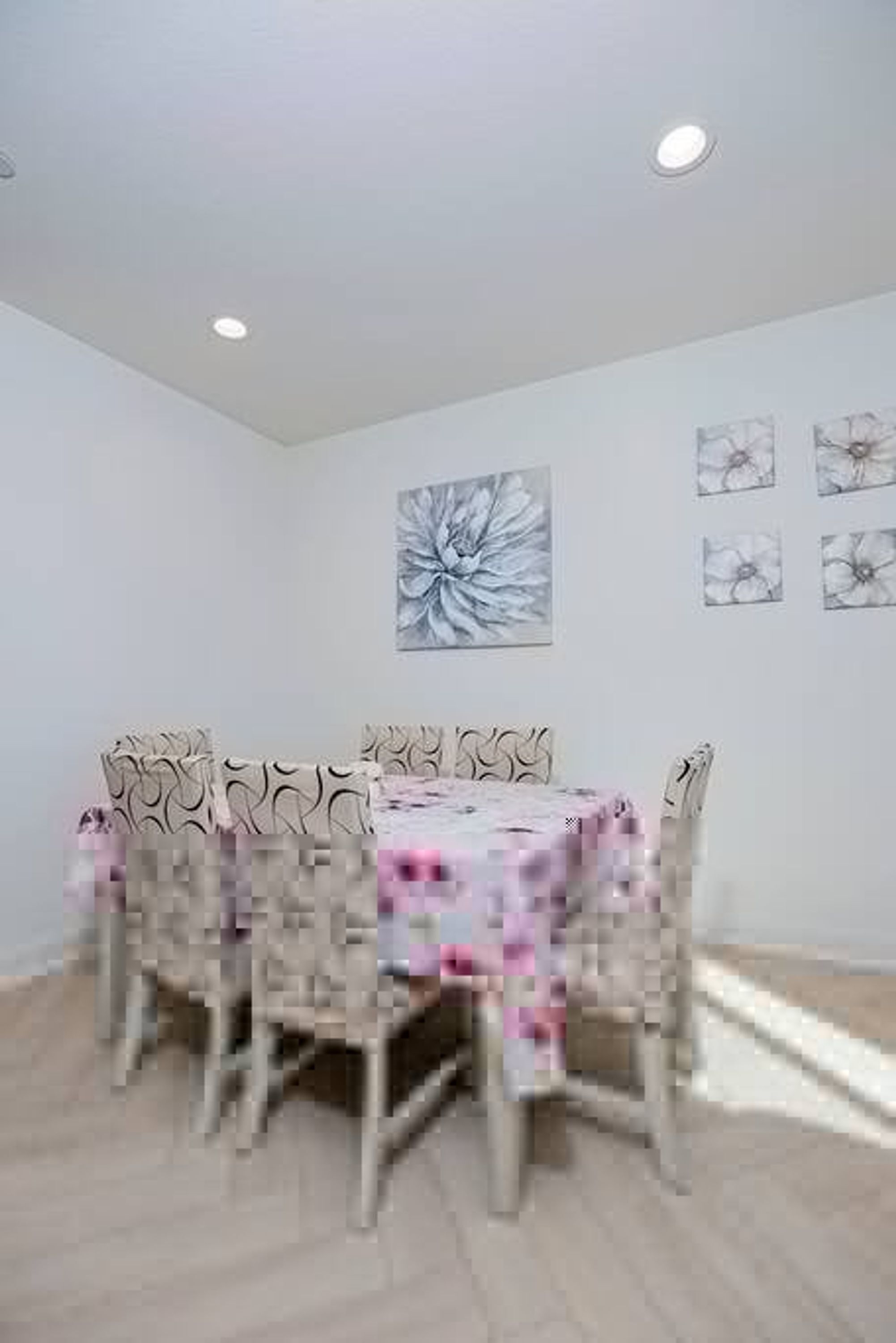 A dining area with a round table and chairs, a floral tablecloth, and wall art.
