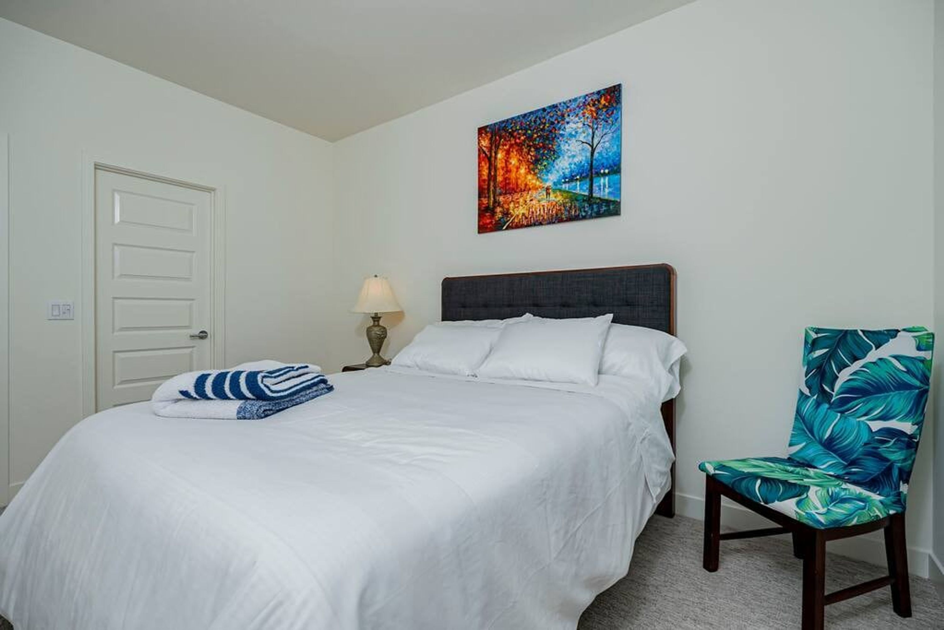 A hotel room with a bed, a chair, a painting, and a door.