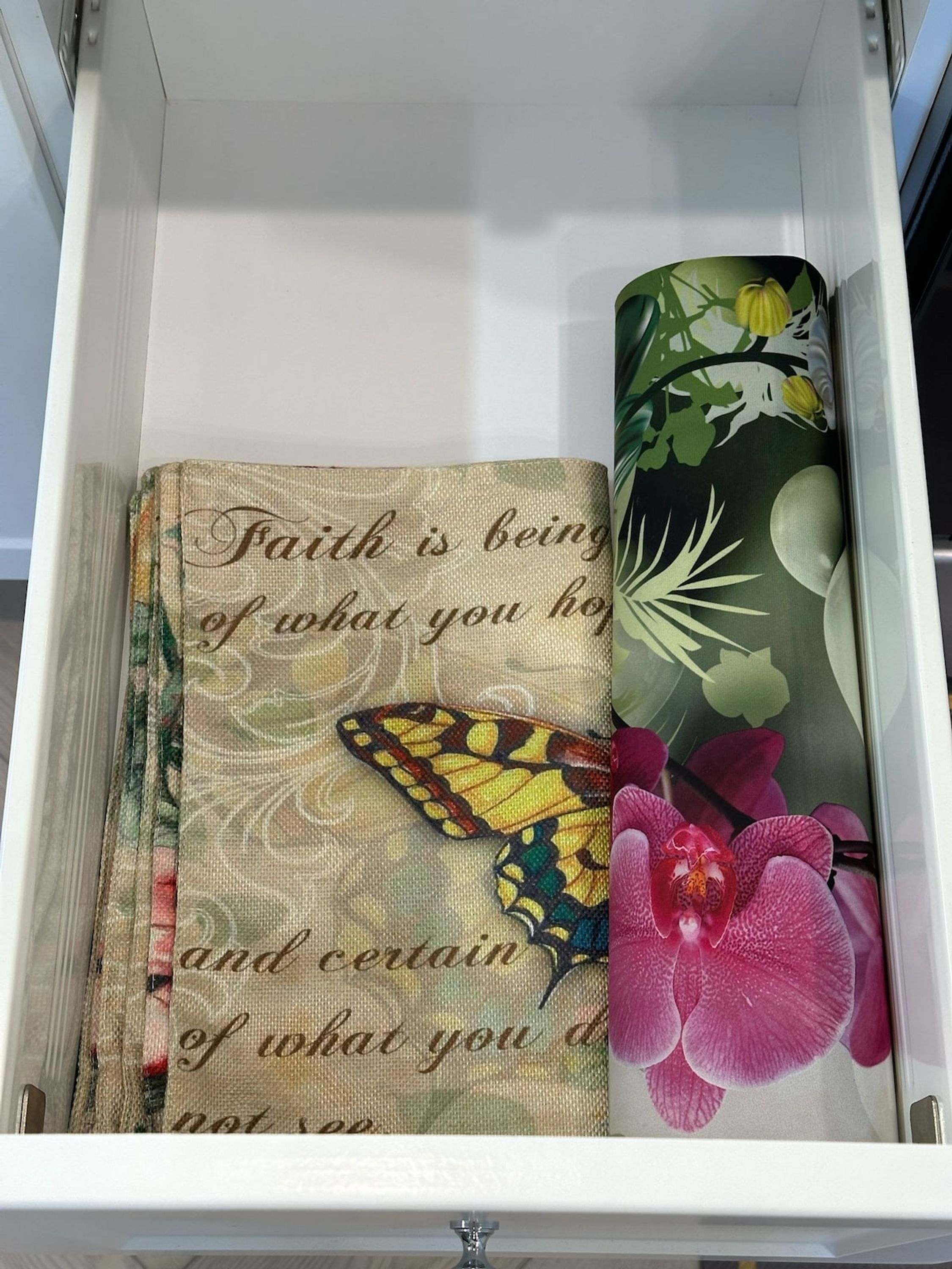 A drawer containing a fabric with a butterfly and floral design, and a rolled-up fabric with a floral pattern.