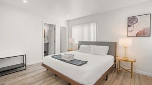 A modern hotel room with a large bed, bedside lamps, a small table, and a painting on the wall. - Modern Family Getaway With Spacious Living Areas (Altadena)