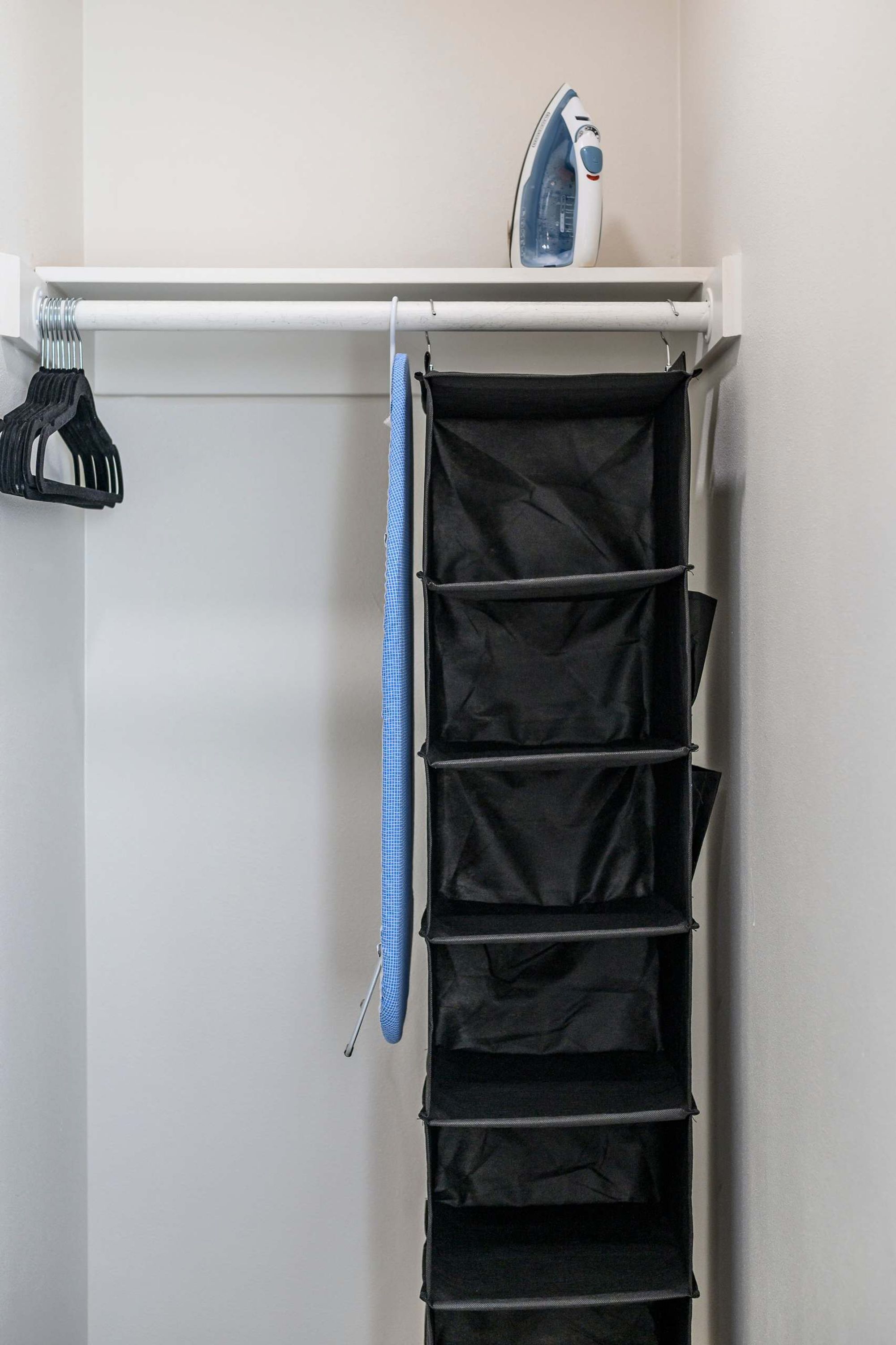 A closet with a hanging rack, an iron, and a blue hanger.
