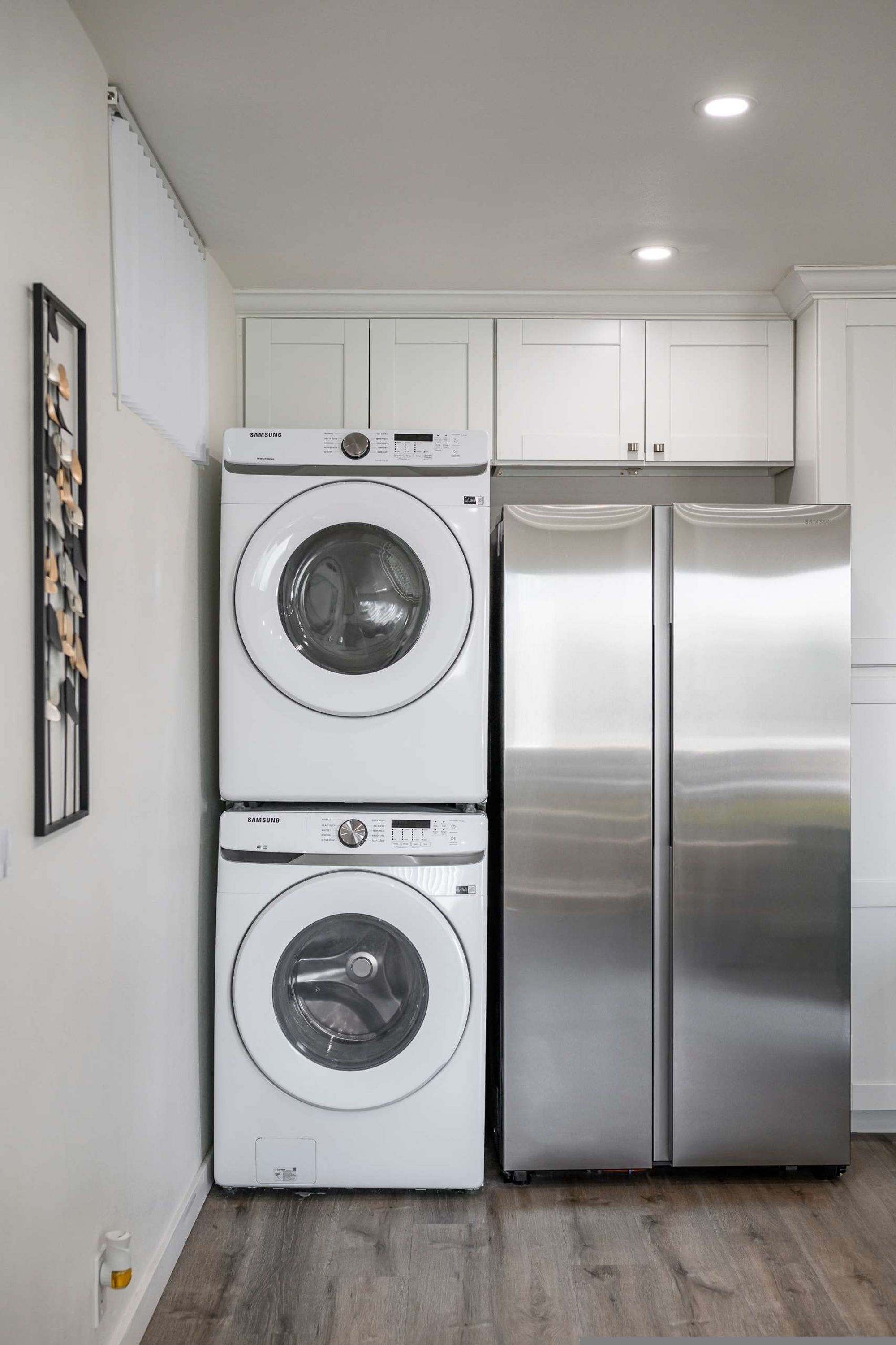 Cocina compacta con lavadora y secadora integradas, refrigerador de acero inoxidable y alacenas blancas.