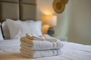 Un lit bien fait, avec des serviettes blanches pliées et une lampe en arrière-plan.