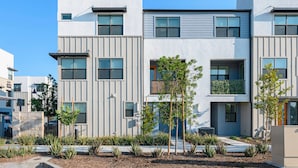 Een modern meerlaags woongebouw met een plat dak, grote ramen en een aangelegde voortuin met jonge bomen en lage struiken.