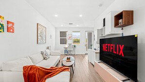 Een moderne woonkamer met een grote flatscreen-tv, een witte bank, een salontafel en een rode plaid.