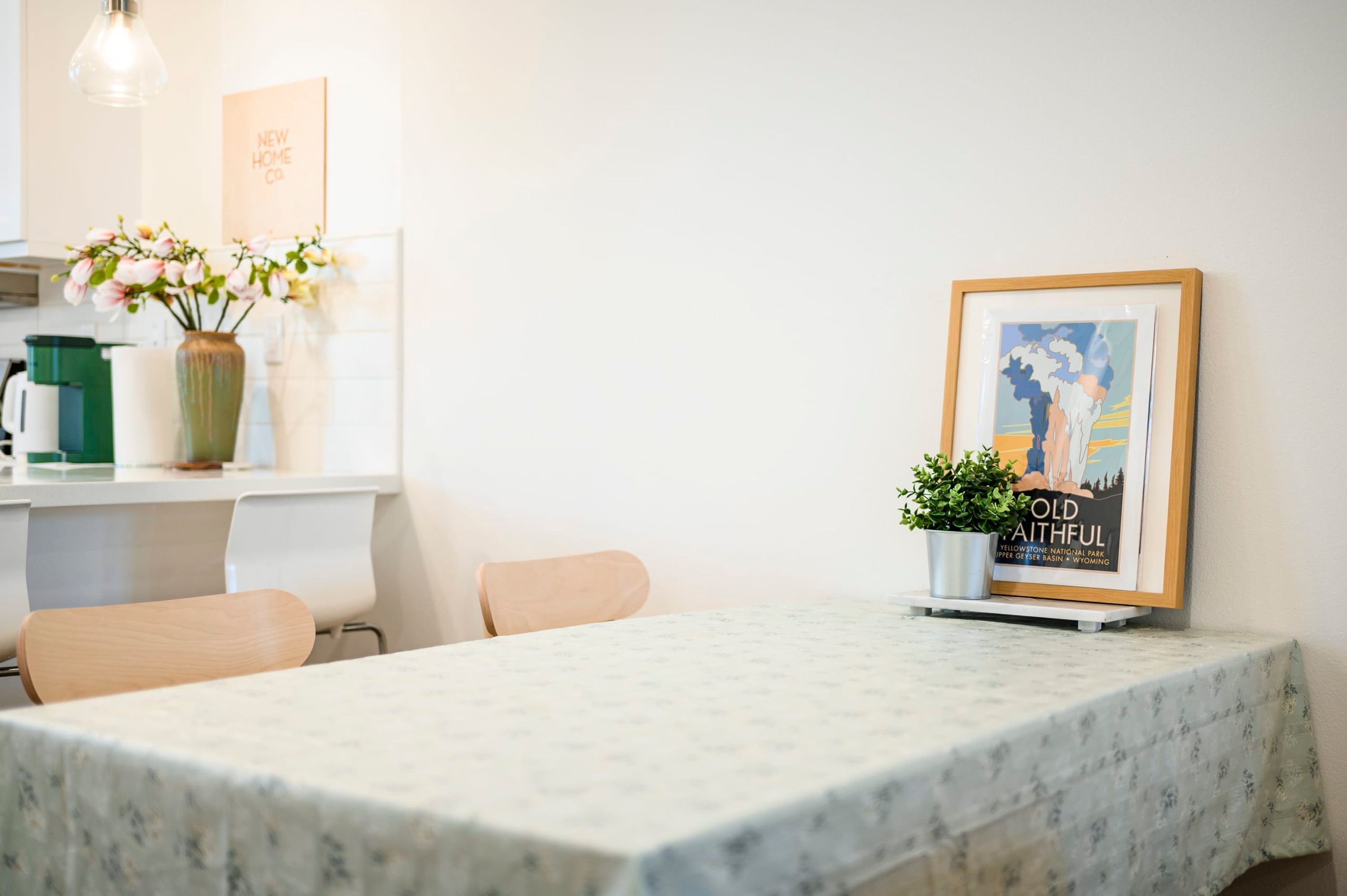 A dining area with a marble table, chairs, a vase with flowers, a framed picture, and a sign on the wall.