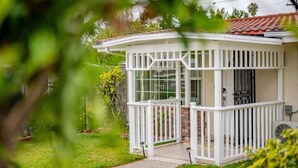 Ein kleines, eingeschossiges Haus mit weißer Fassade, einer Veranda und einem Ziegelkamin.