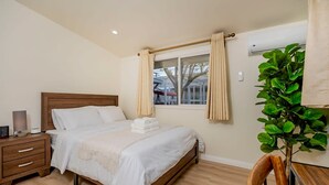 Ein Schlafzimmer mit einem hölzernen Bett, einem Nachttisch, Vorhängen an einem Fenster und einer Topfpflanze.