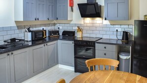 A modern kitchen with grey cabinets, a black stove, a microwave, and a toaster. There is a wooden table and chairs in the center.