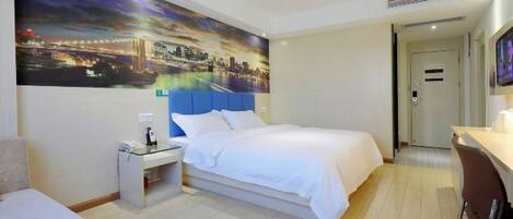 Habitación de hotel con cama, escritorio, silla, mesita de noche y un cuadro grande con una vista urbana.
