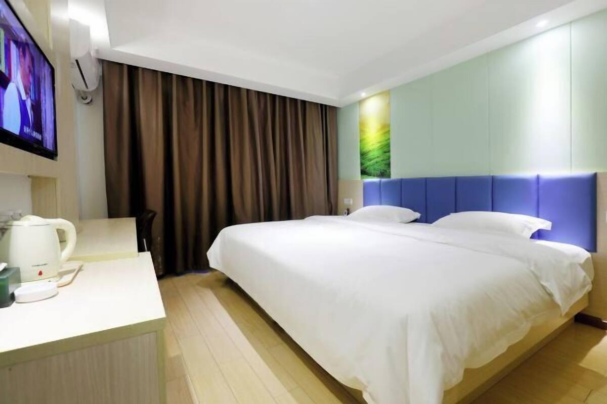 Una habitación de hotel con cama, escritorio, televisor y ventana con cortinas.