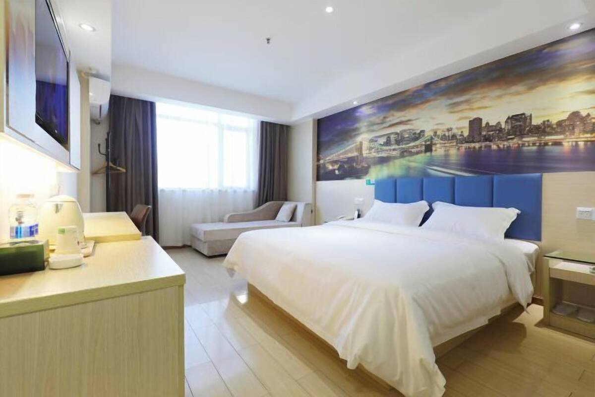 Habitación de hotel con cama, escritorio, silla, televisión y una pintura de paisaje urbano en la pared.