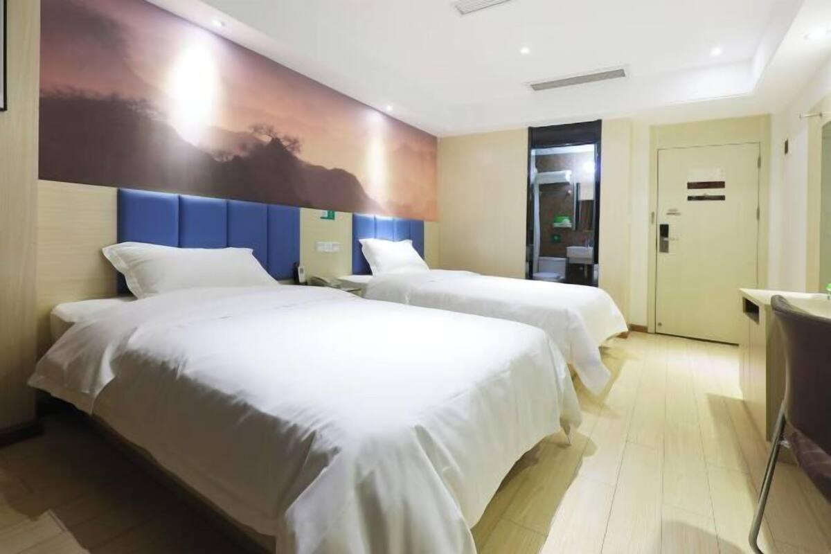 Habitación de hotel con dos camas, un mural grande en la pared, un baño con puerta de cristal y un escritorio pequeño.