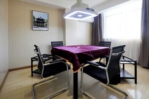 Un comedor con una mesa cubierta por un mantel morado, rodeada por cuatro sillas negras con estructura metálica. Una lámpara colgante moderna ilumina la mesa.