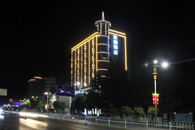A multi-story hotel with illuminated signage, a prominent vertical structure, and a street view with a fence and streetlights.
