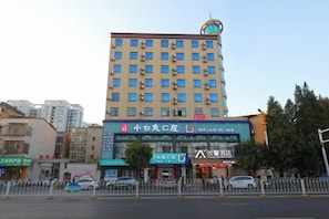A multi-story hotel with a prominent signboard, several ground-level shops, and a fenced parking area.