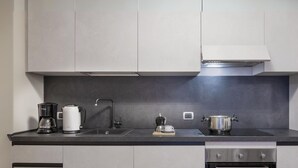 Moderni keittiö, jossa on tumma työtaso, kahvinkeitin, vedenkeitin, kattila ja pesuallas.