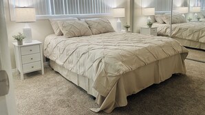 A bedroom with a large bed, two bedside tables, a mirror, and a window with blinds. - Soothing Beach Apartment in Redondo Beach…20 steps to Ocean! (Redondo Beach)