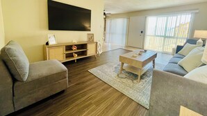 A living room with a flat-screen TV, a wooden entertainment unit, and a sofa. - Soothing Beach Apartment in Redondo Beach…20 steps to Ocean! (Redondo Beach)