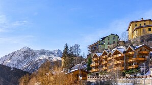 A mountain lodge with multiple wooden cabins and a large yellow building with balconies, surrounded by snow-covered mountains.