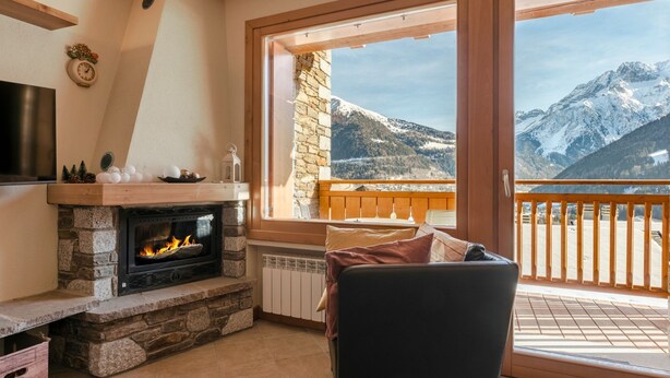 A cozy room with a fireplace, a comfortable seating area, and a balcony with a mountain view.
