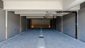 A long, empty corridor with grey metal doors on both sides and a blue tiled floor.