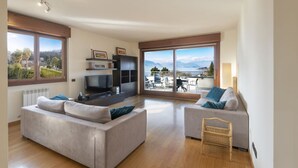 A modern living room with a sofa, a TV, and a balcony with a view of the mountains. - The House on the Lake (Reno)