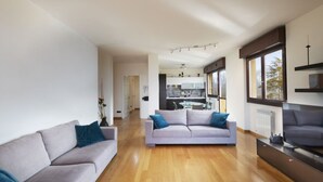 A modern living room with a grey sofa and a smaller grey couch, both with blue cushions. A wooden floor and a kitchen area are visible in the background. - The House on the Lake (Reno)