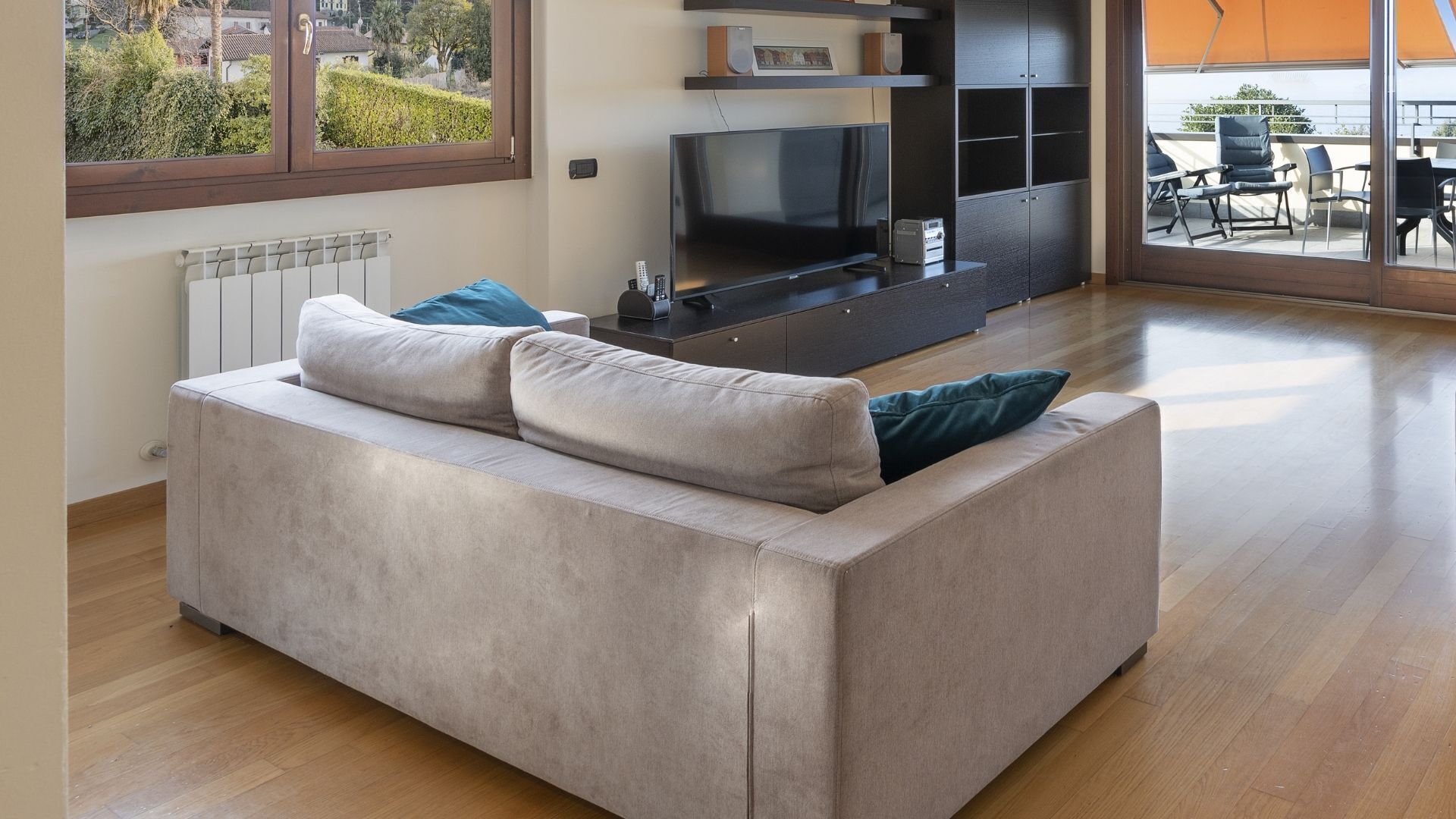 Un salon moderne avec un canapé beige, un téléviseur à écran plat et une vue sur l’extérieur grâce à une grande fenêtre.