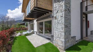 Une maison moderne avec une façade en pierre, de grandes portes-fenêtres coulissantes et une terrasse en bois.
