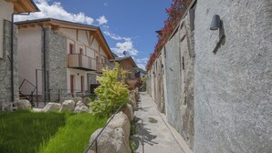 Une ruelle étroite, bordée de bâtiments aux murs de pierre, avec une rambarde en métal et un chemin.