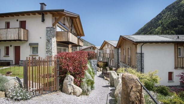 Un bâtiment de style chalet traditionnel, doté d’une façade en pierre, de balcons en bois et d’un chemin de gravier menant à l’entrée.