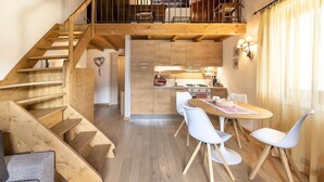 A wooden staircase leading to a lofted dining area with white chairs and a kitchen in the background. - Sunshine - Two Bedroom Apartment, Sleeps 4 (Vione)